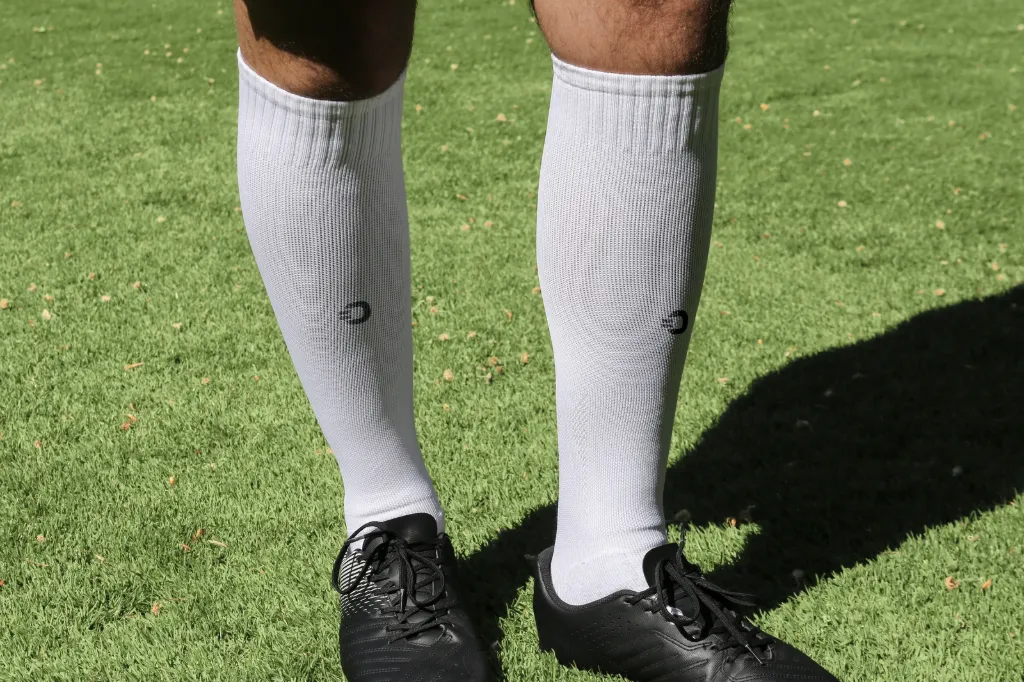 Vorderansicht der getragenen weißen HOLIES Socken auf dem Fußballplatz.