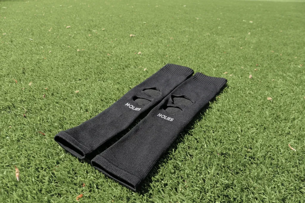 Ein Paar schwarze Cut Sleeves mit offenen Abschlüssen, flach auf Rasen ausgelegt.
